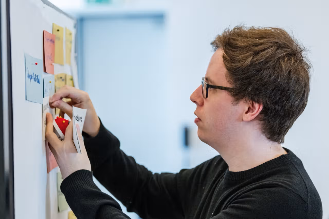 Conciso-Kollege heftet Karten und Sticky-Notes an ein Whiteboard und ordnet einen Prozessablauf
