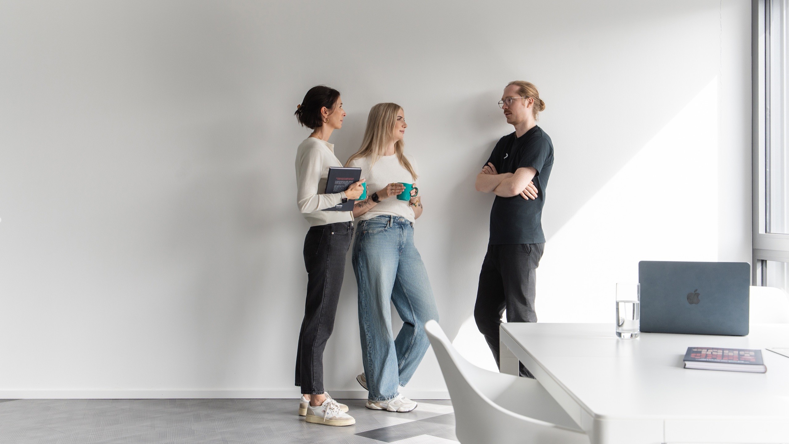 Drei Menschen stehen im Gespräch an einer Wand in einem hellen, minimalistischen Büro