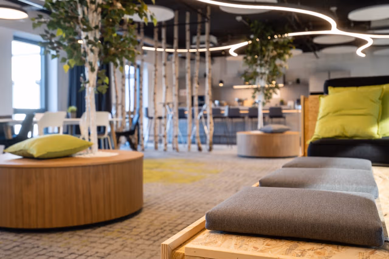 Offener Lounge-Bereich im Conciso-Büro mit Sitzinseln, Birkenstämmen und grünen Kissen