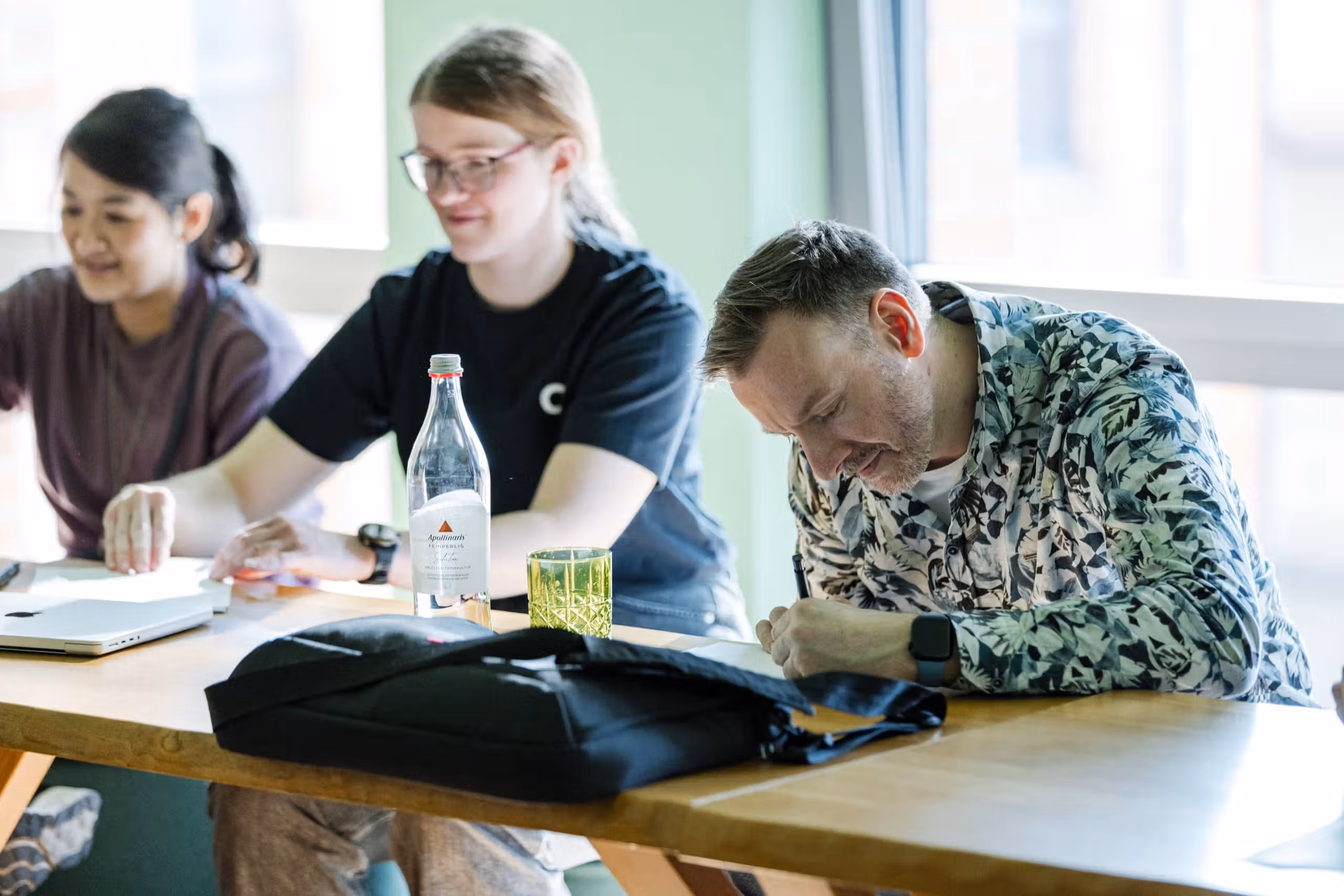 Drei Personen arbeiten im hellen Workshop-Raum gemeinsam am Tisch mit Laptops