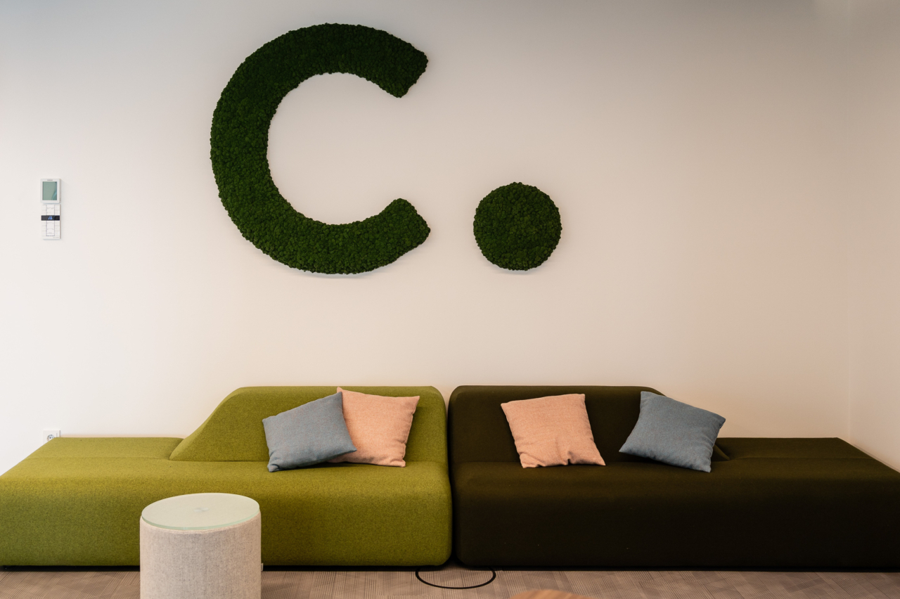 Zu sehen sind zwei grüne Sofas im Eingangsbereich der Conciso GmbH. Über den Sofas hängt das Conciso-Logo.